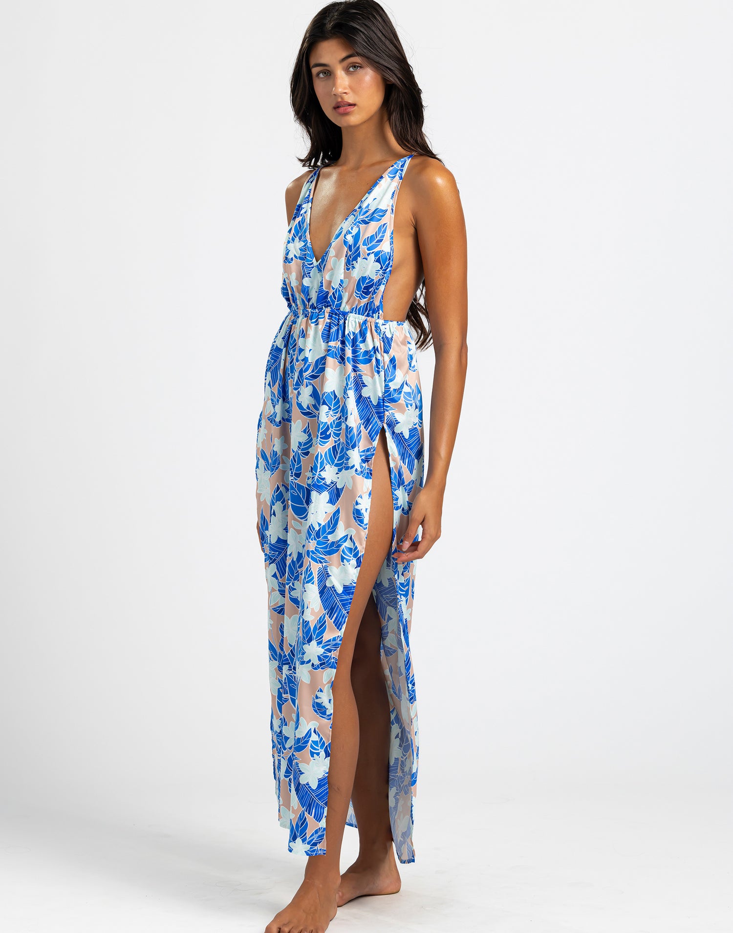 The model is wearing the Campbell Maxi Dress, a sleeveless dress with a deep V-neckline and a vibrant blue floral print. The dress has a flowy silhouette with high side slits, creating an elegant and breezy look.