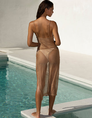 A woman standing by a pool wearing a sheer, tan mesh midi dress with thin straps. The dress has a side slit and reveals a swimsuit underneath. She poses confidently with a relaxed expression, her wet hair cascading over her shoulders, against a minimalist, sunlit backdrop.
Back