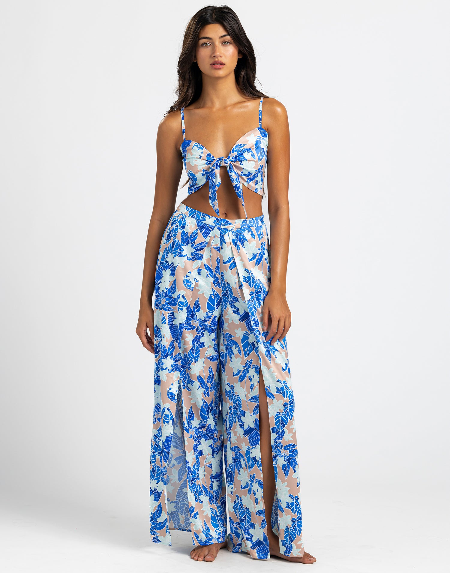 The model is wearing the Ramsey Pants  of wide-leg pants featuring a vibrant blue floral print on a light background. The pants have a flowy design with high slits, offering a breezy and elegant style perfect for summer.