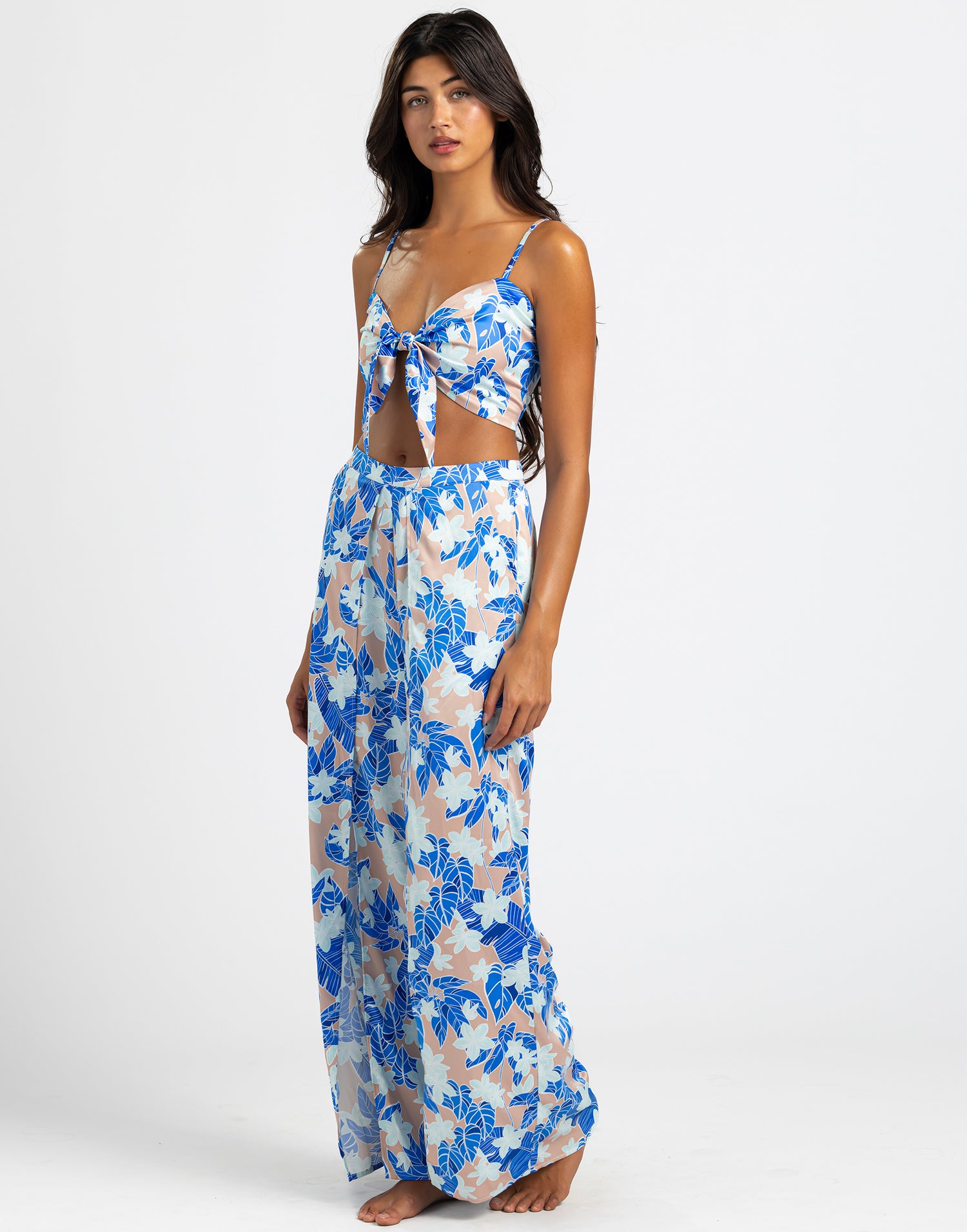 The model is wearing the Ramsey Pants  of wide-leg pants featuring a vibrant blue floral print on a light background. The pants have a flowy design with high slits, offering a breezy and elegant style perfect for summer.